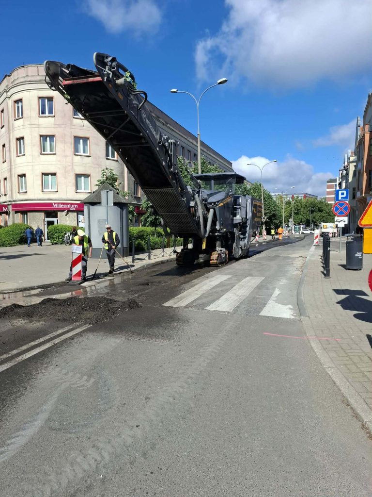 Robot drogowy prowadzi prace na ul. Mickiewicza w centrum Olsztyna, wokół trwają roboty drogowe.
