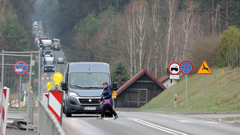 Kobieta przechodzi przez jezdnię w pobliżu znaków drogowych, z samochodami w tle na drodze krajowej nr 51.