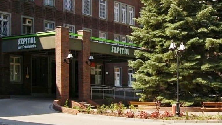 Widok z zewnątrz szpitala psychiatrycznego we Fromborku, wejście do placówki z zielonym napisem "Szpital".