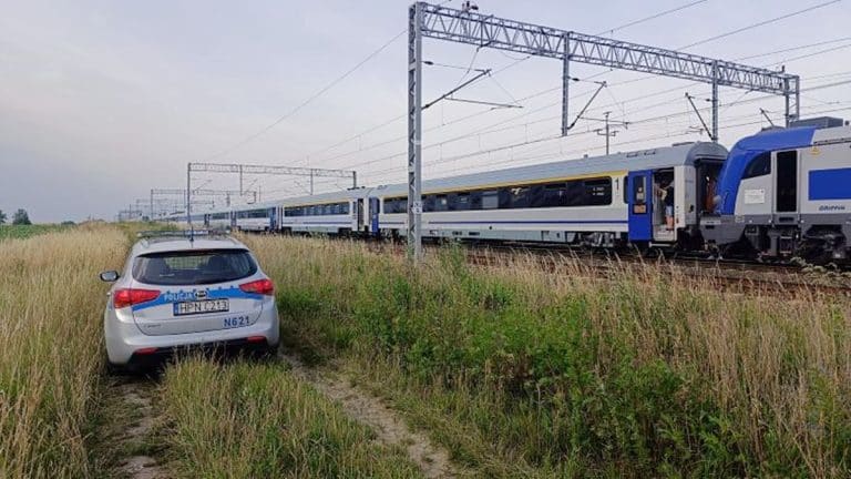 Pociąg relacji Kraków–Olsztyn na torach, obok policyjny samochód na polu, wypadek w Olsztynku.