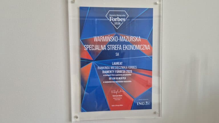 Certyfikat Diamentów Forbesa 2026 dla Warmińsko-Mazurskiej Specjalnej Strefy Ekonomicznej, na białej ścianie.