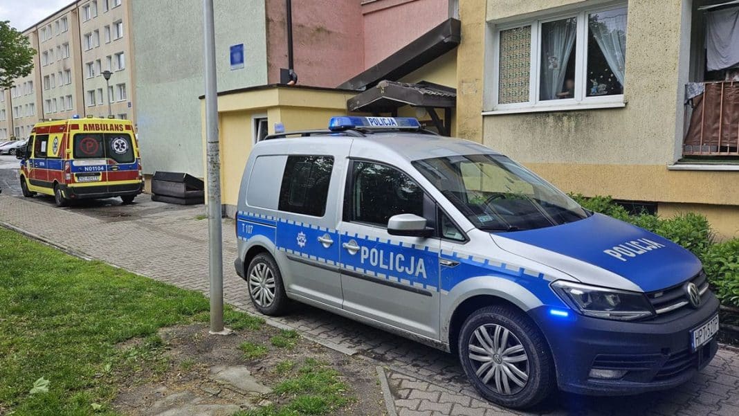 Na zdjęciu radiowóz policji i ambulans zaparkowane przed blokiem mieszkalnym w Iławie.