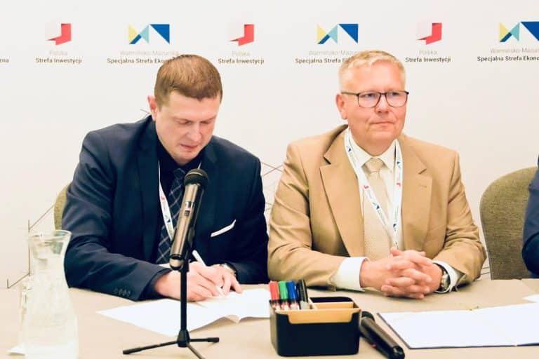 Dwóch mężczyzn podczas konferencji, za nimi logo Strefy Ekonomicznej na ścianie.
