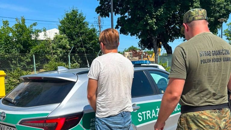 Strażnik graniczny i osoba w białej koszulce przy samochodzie policyjnym na drodze.