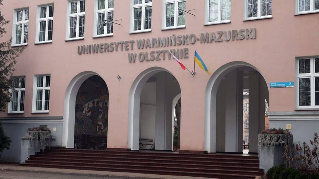 Budynek rektoratu Uniwersytetu Warmińsko-Mazurskiego z flagami Polski i Ukrainy na fasadzie.