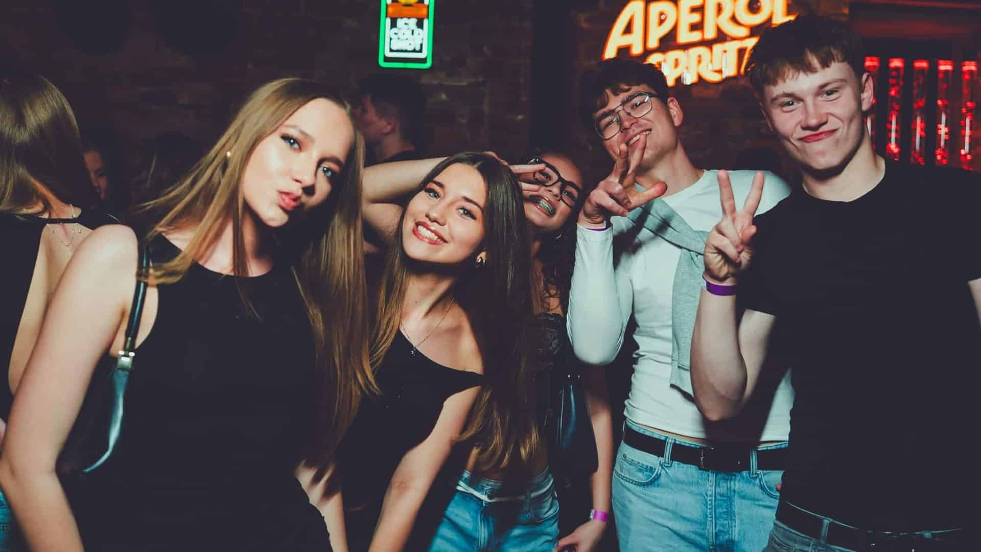 Grupa młodych ludzi bawi się na imprezie w klubie nocnym, uśmiechając się i pozując do zdjęcia.