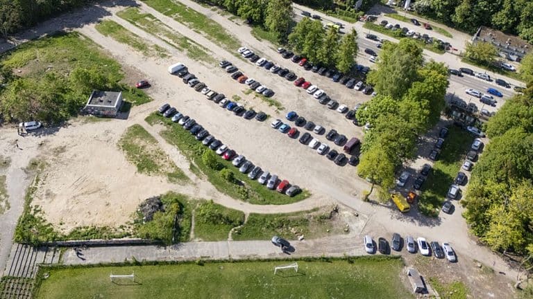 Widok na wyłączony z użytkowania parking przy al. Sybiraków w Olsztynie, z samochodami i drzewami wokół.