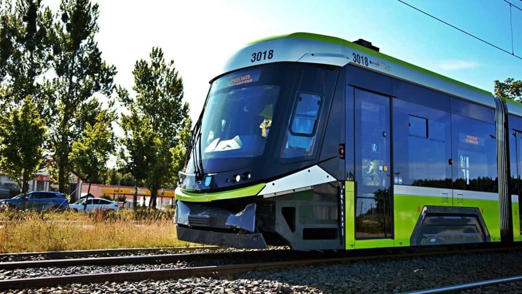 Nowoczesny tramwaj na torach w Olsztynie, w tle drzewa i budynki.