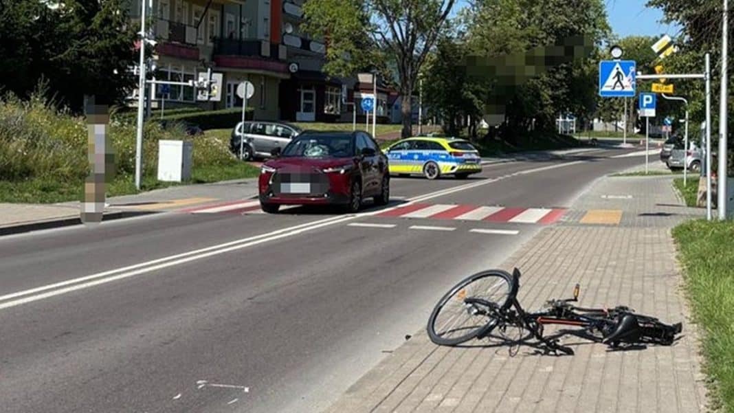 Rowerzysta leży na chodniku po wypadku, w tle samochód i policja na ulicy.