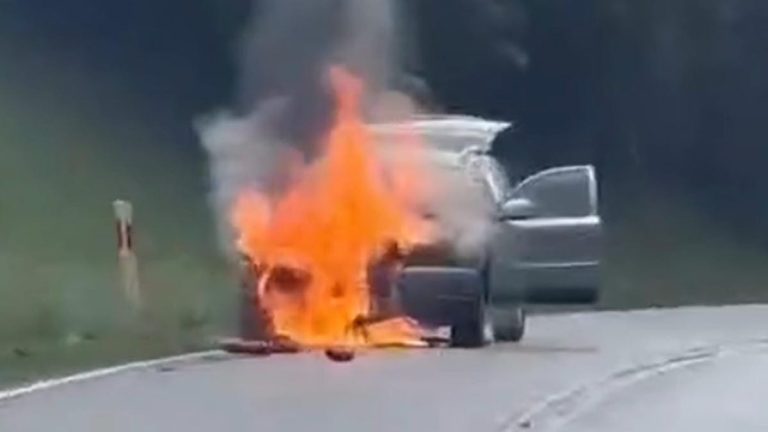 Samochód płonie na drodze krajowej, widoczne wysokie płomienie i dym.