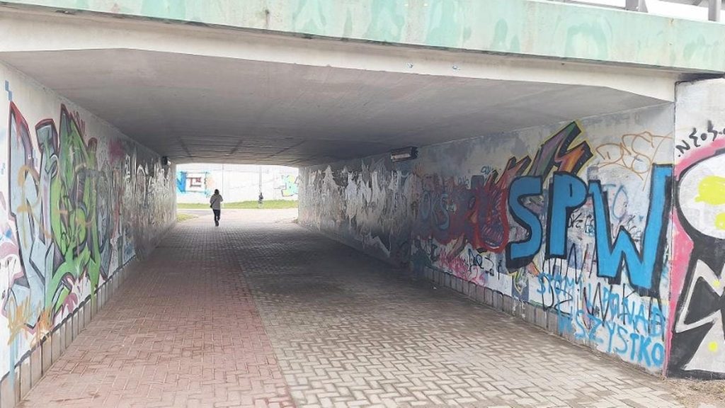 Podziemny przejazd pod ulicą ozdobiony graffiti i muralami, z widocznym przejściem dla pieszych.