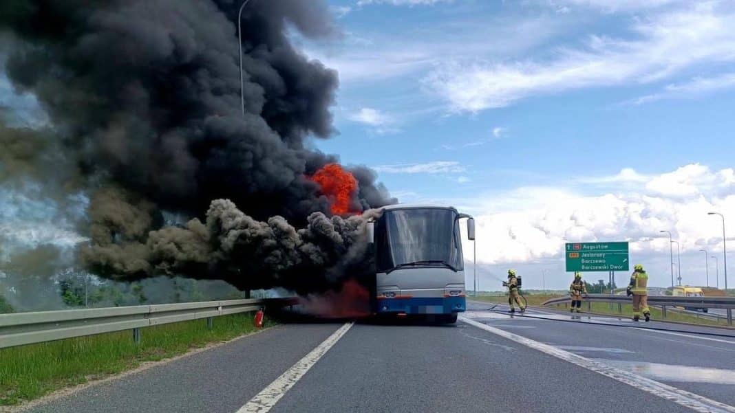 Pożar autobusu na drodze krajowej nr 16 pod Olsztynem, widoczny dym i ogień z pojazdu, strażacy na miejscu.