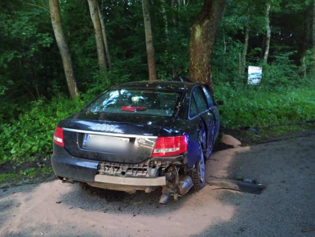 Rozbity samochód marki Audi na poboczu, w środku śpiący młody mężczyzna, otoczony lasem.