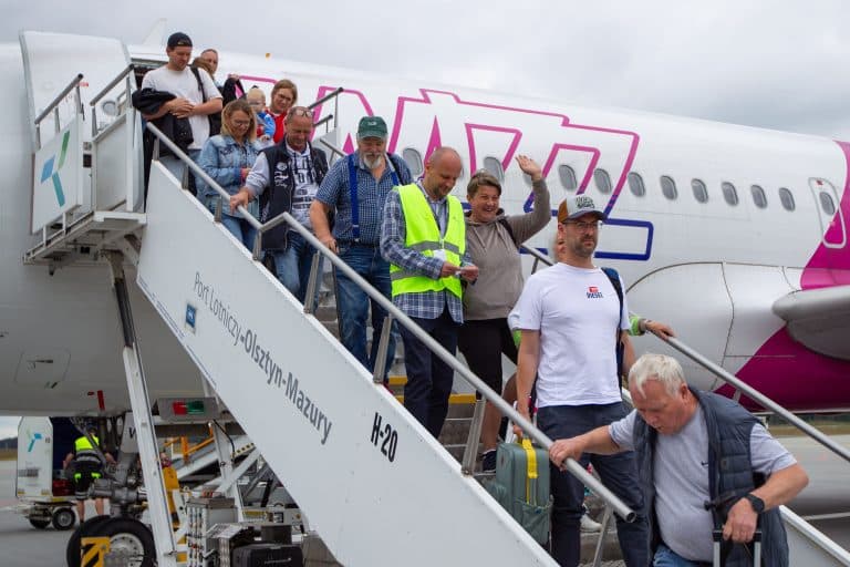 Grupa pasażerów schodzi z samolotu na lotnisku w Szymanach, w tle widać samolot Wizz Air.