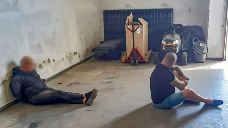 Dwoje osób siedzi na podłodze w pomieszczeniu, w tle narzędzia i sprzęt sprzątający.
