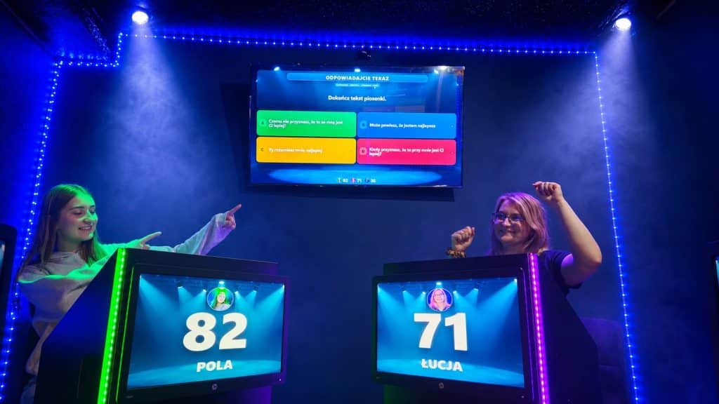 Dwie dziewczyny grają na interaktywnych matach LED w centrum Olsztyna, na ekranie teleturniejowe pytanie.