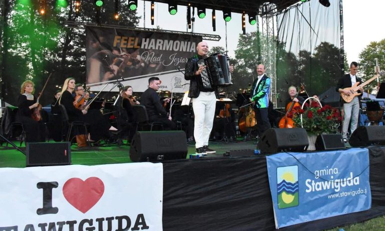 Orkiestra na scenie podczas koncertu nad Jeziorem Wulpińskim, widoczne instrumenty i muzycy.