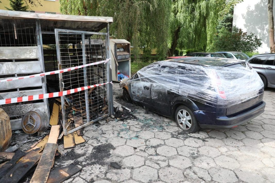 Uszkodzony samochód i zniszczona wiatka śmietnikowa po pożarze na osiedlu w Olsztynie.