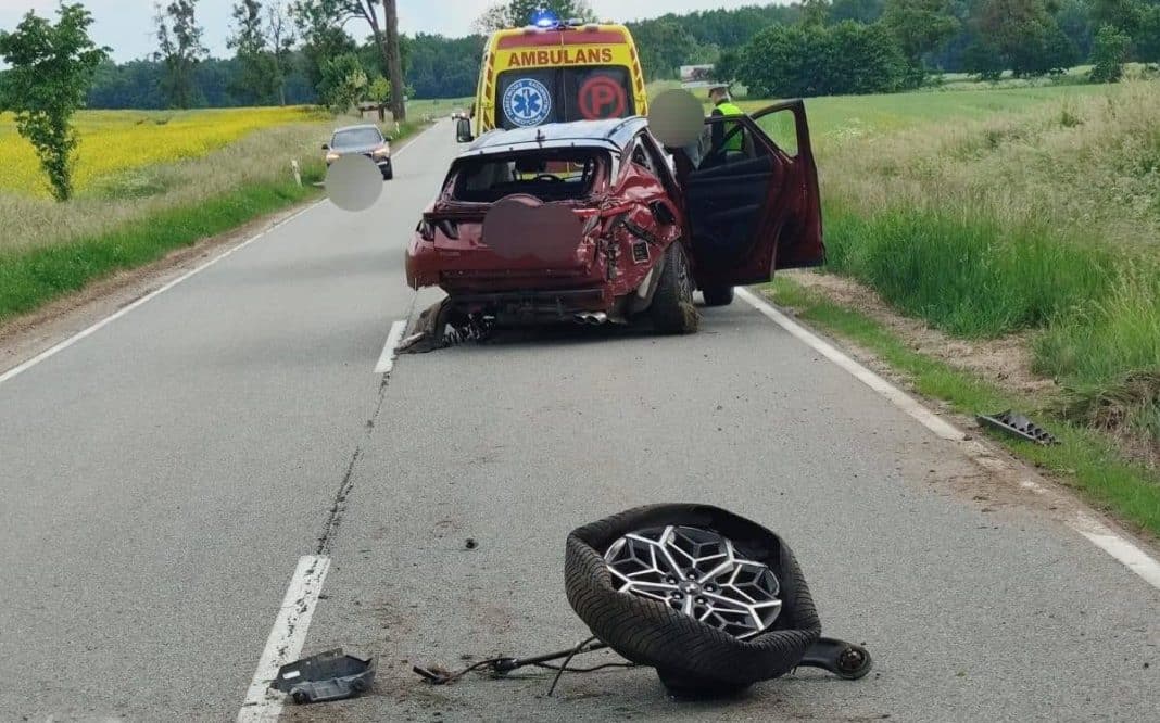 Rozbity samochód na drodze krajowej nr 57 po wypadku, leżące koło i służby ratunkowe w tle.