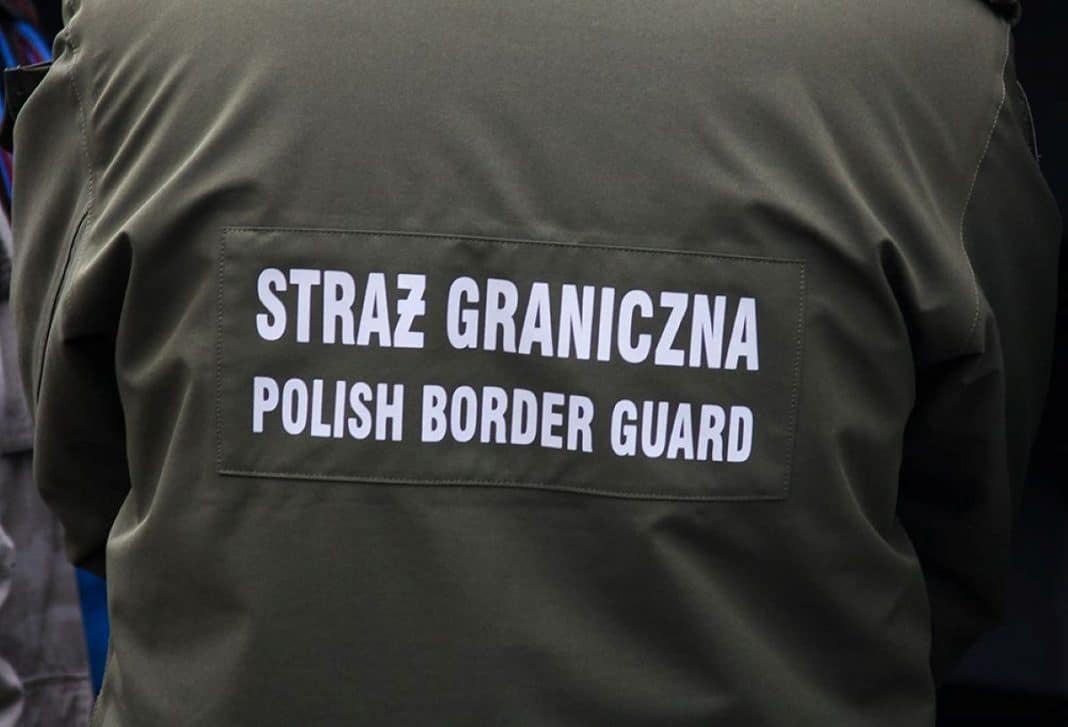 Osoba w kamizelce z napisem Straż Graniczna, widoczna z tyłu, na lotnisku w Szymanach.
