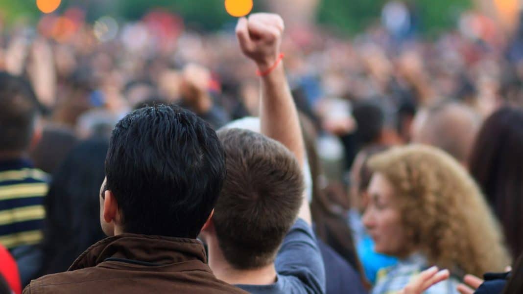 Grupa ludzi na demonstracji, jedna osoba podnosi pięść w geście protestu.