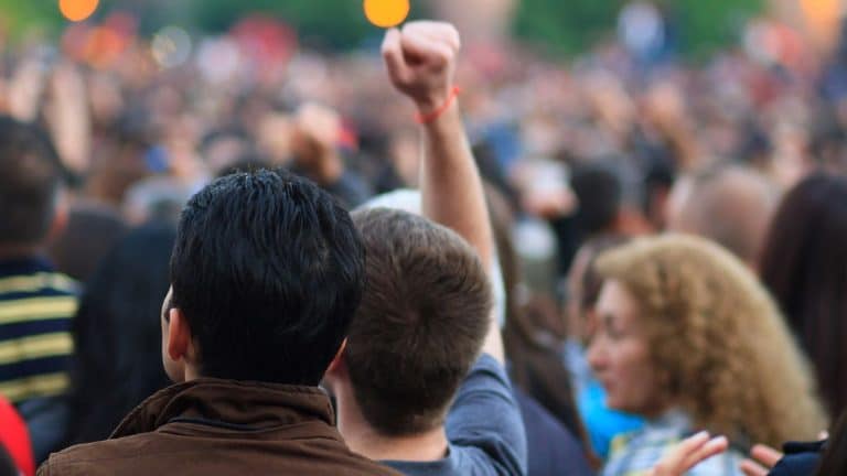 Grupa ludzi na demonstracji, jedna osoba podnosi pięść w geście protestu.