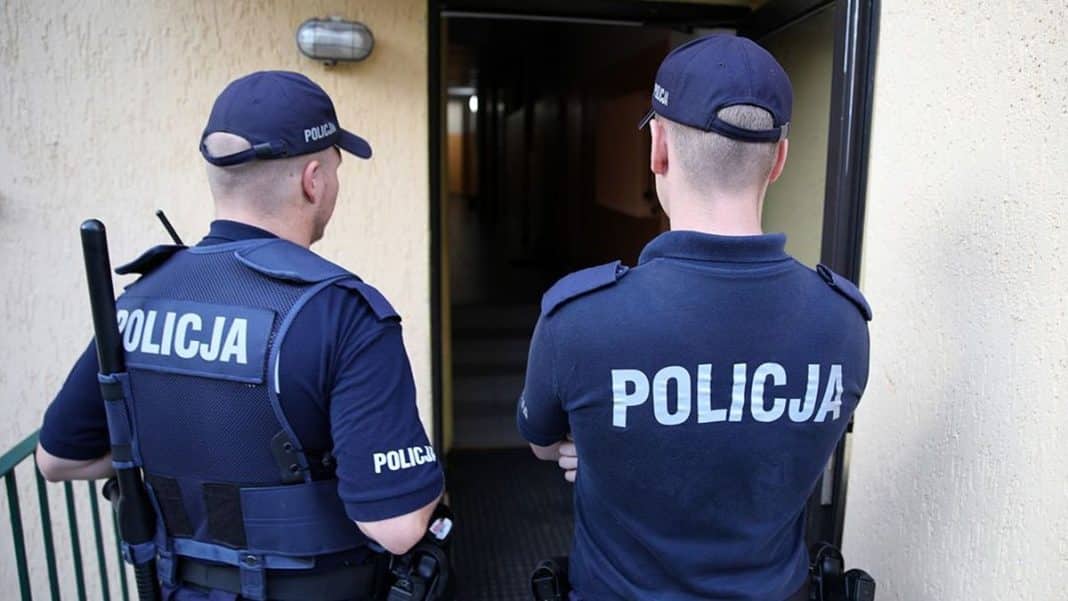 Dwóch policjantów stoi przed wejściem do budynku, patrząc na monitoring.