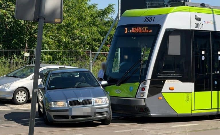 Zderzenie tramwaju z samochodem osobowym przy dworcu głównym w Olsztynie, widok na tramwaj i auto na ulicy.