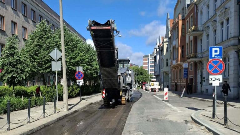Robot drogowy pracuje na ulicy Mickiewicza w centrum Olsztyna podczas remontu, wokół drzewa i budynki.