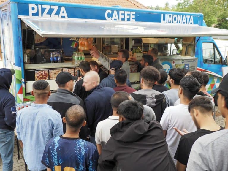 Grupa ludzi czekających przy kolorowym food trucku z pizzą na Mazurach.