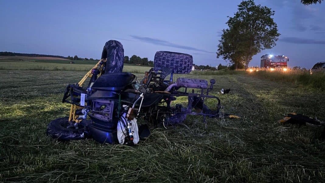 Zniszczony quad leży na polu po wypadku, w tle pojazd straży pożarnej i drzewo, wieczorem.