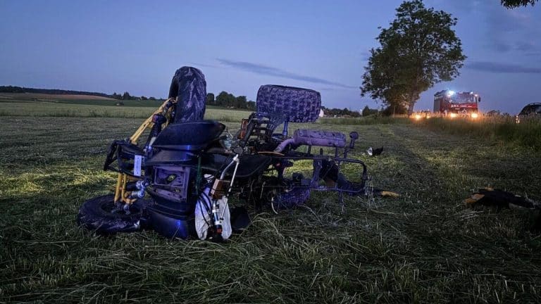 Zniszczony quad leży na polu po wypadku, w tle pojazd straży pożarnej i drzewo, wieczorem.