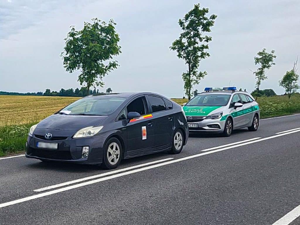 Samochód marki Toyota zatrzymany na drodze krajowej nr 16 przez służby, obok stoi radiowóz.