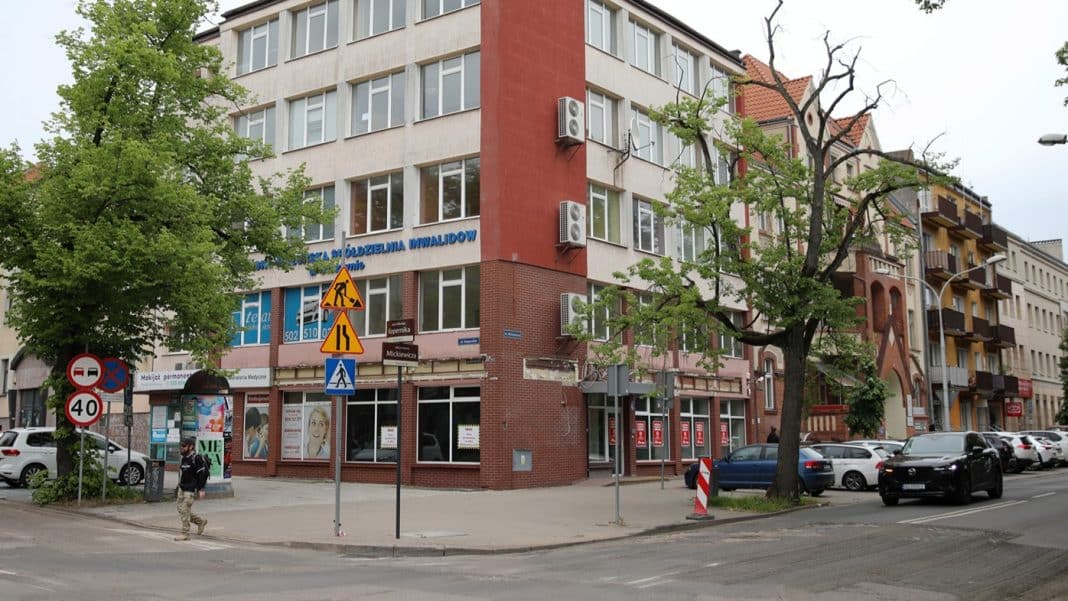Widok na wielopiętrowy budynek przy ul. Kopernika 46A w Olsztynie, z drzewami i samochodami na ulicy.