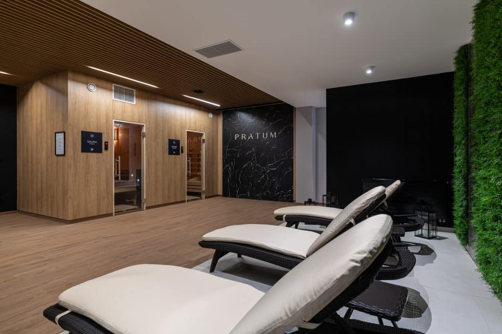 Relaksacyjne leżaki w nowoczesnym spa z saunami, wnętrze z drewnianymi panelami i zieloną ścianą.