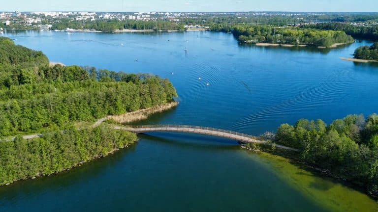 Widok na Jezioro Ukiel z kładką pieszo-rowerową nad cieśniną „Lwia Paszcza”, otoczoną zielonymi terenami.