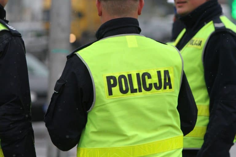 Policjant w kamizelce odblaskowej z napisem 'Policja' na tle innych funkcjonariuszy.