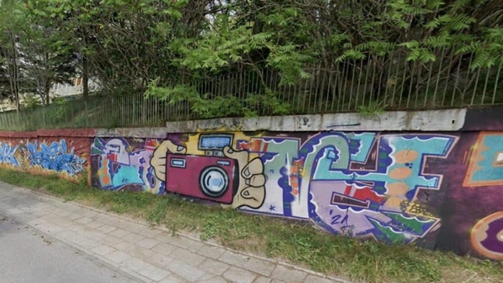 Graffiti na murze przy ulicy, przedstawiające kamerę i kolorowe litery.