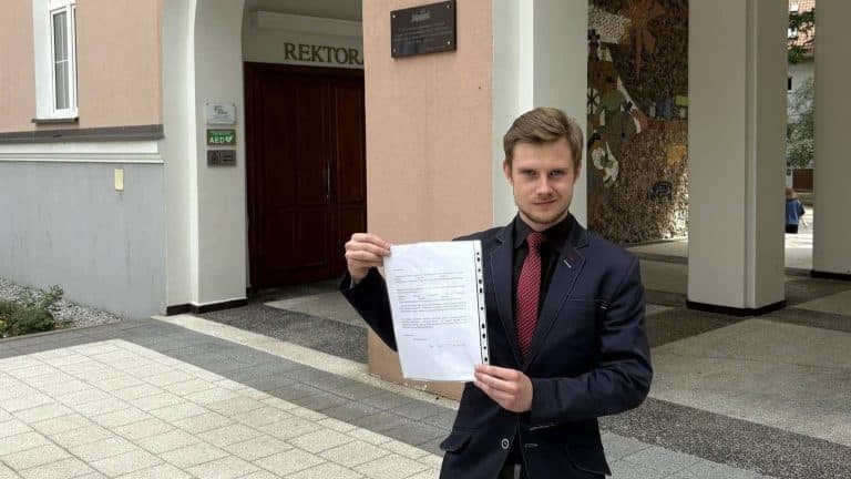 Mężczyzna w garniturze trzyma dokument przed budynkiem rektoratu UWM.