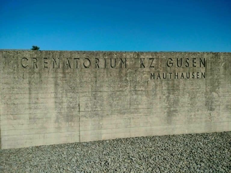 Betonowa ściana z napisem 'Cmentarz KZ Gusen' na tle nieba.