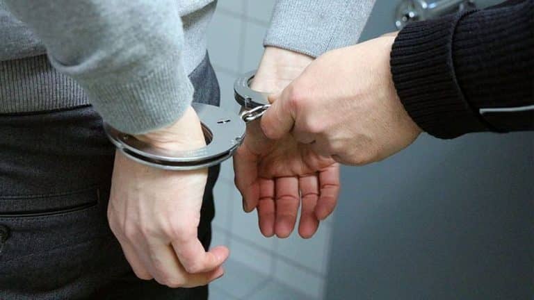 Osoba w rękawiczkach jest zatrzymywana i zakładane są jej kajdanki.