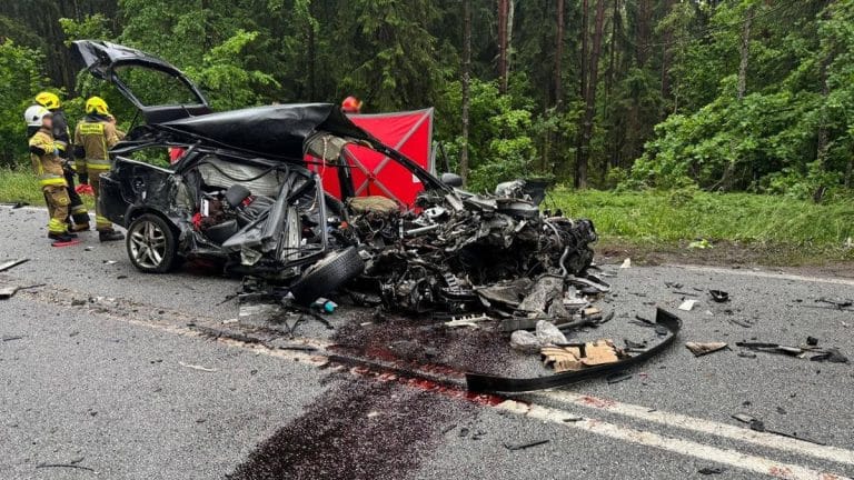 Zniszczony samochód osobowy po wypadku na drodze krajowej nr 16, w pobliżu lasu, z widocznymi służbami ratunkowymi na miejscu.