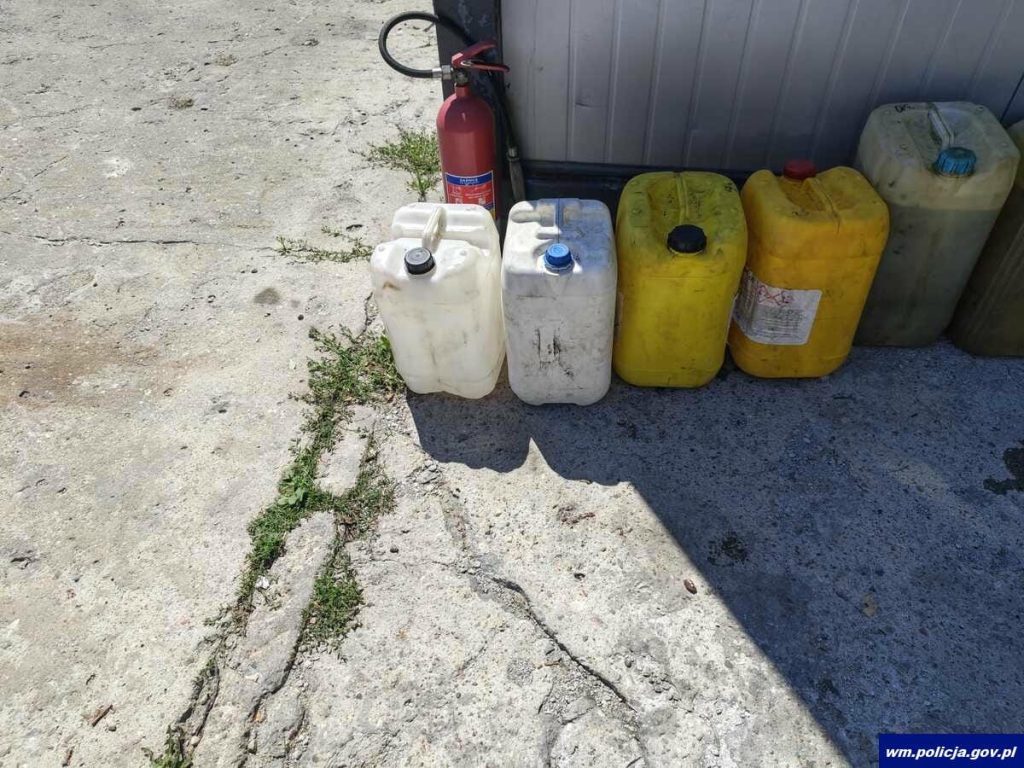Zbiór plastikowych kanistrów i gaśnica ustawione przy ścianie budynku.