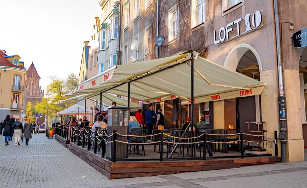 Restauracja Loft 2.0 z zadaszonym tarasem na starówce w Olsztynie, z ludźmi siedzącymi przy stolikach.