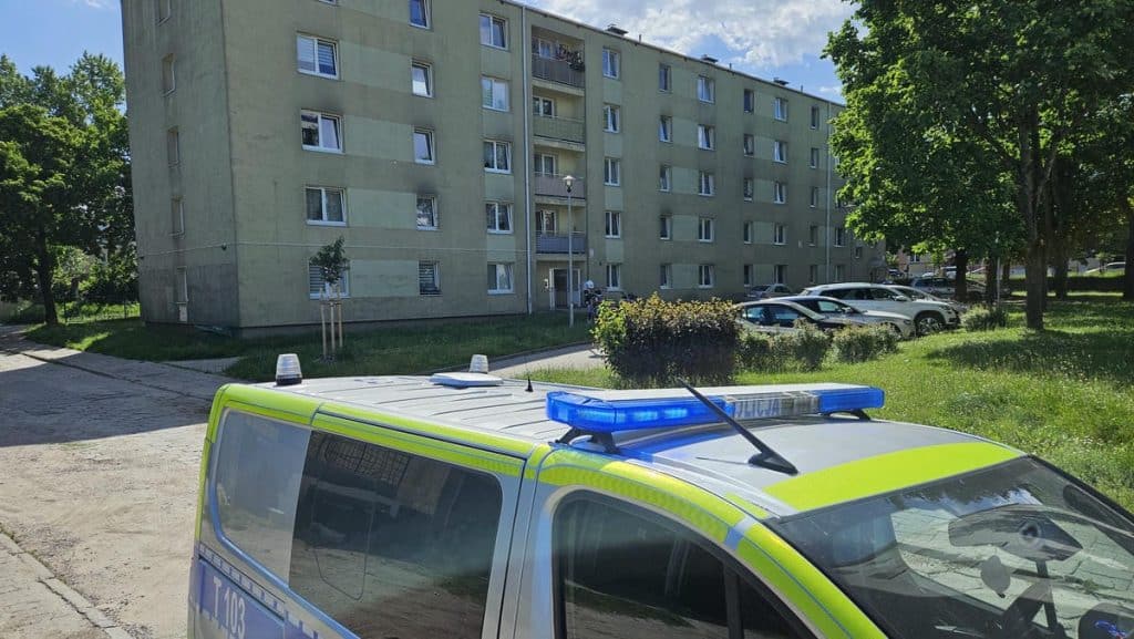 Na zdjęciu widoczny jest radiowóz policyjny na tle bloku mieszkalnego w zielonym otoczeniu.