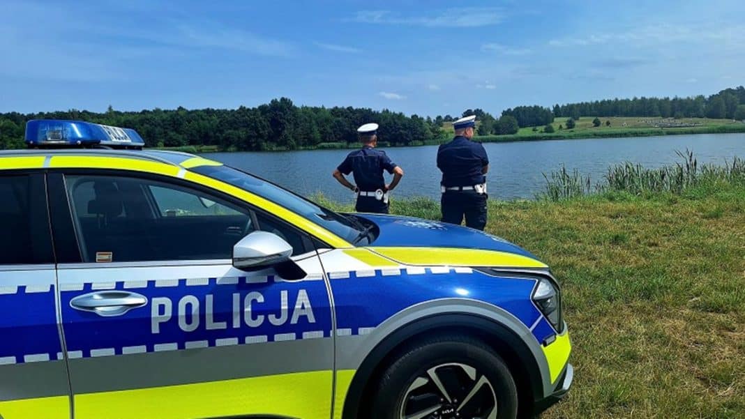 Policjanci na brzegu jeziora Nidzkiego, w tle woda i zalesione brzegi.