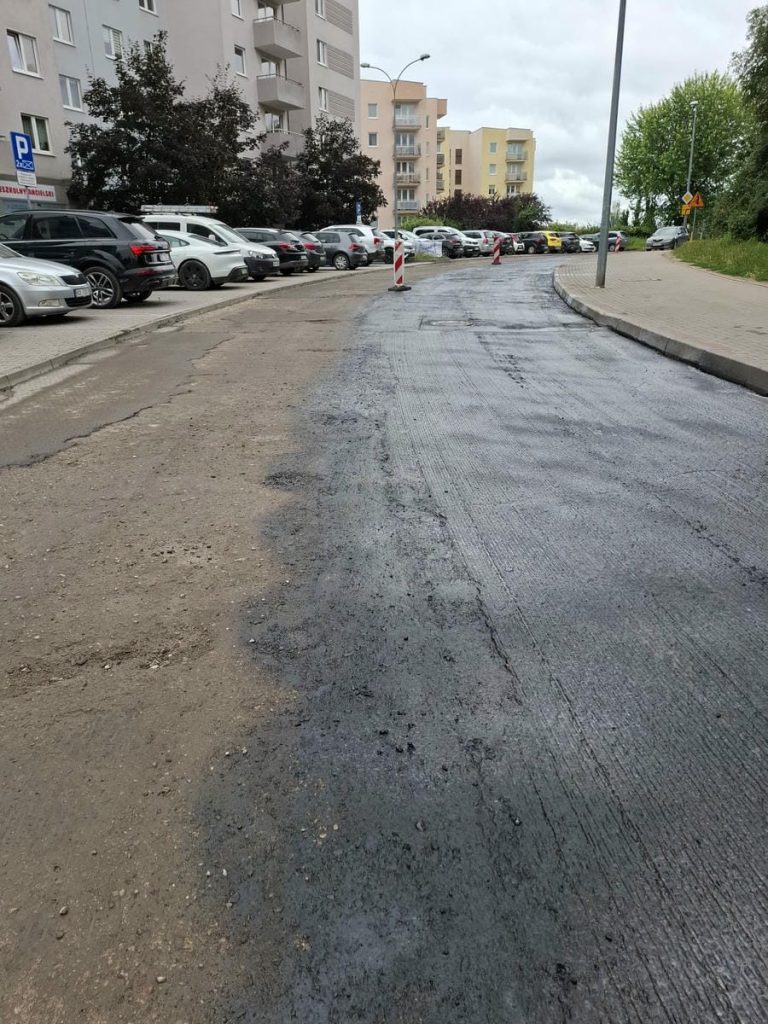 Ulica Barcza w Olsztynie z zamkniętym przejazdem i parkingiem, w tle bloki mieszkalne i drzewa.