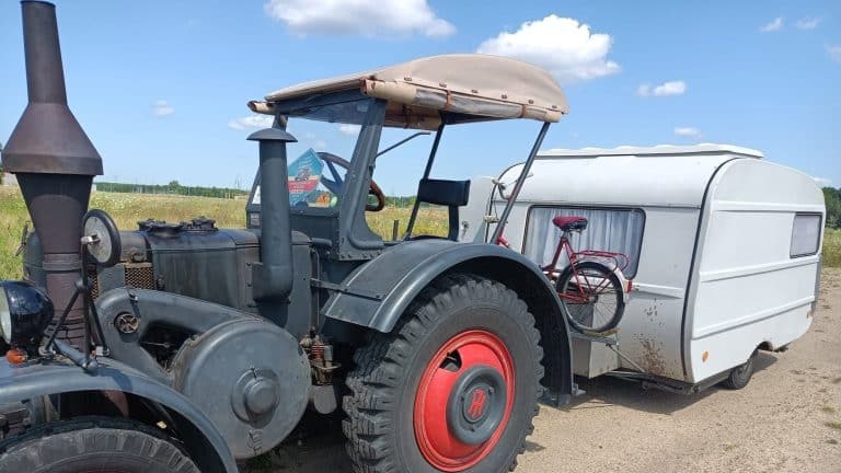 Ciągnik rolniczy z przyczepą kempingową na drodze ekspresowej S61, w tle niebo z chmurami.