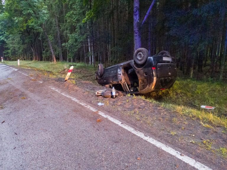 Rozbity samochód na poboczu drogi w lesie, wypadek samochodowy, policja i służby ratunkowe na miejscu.