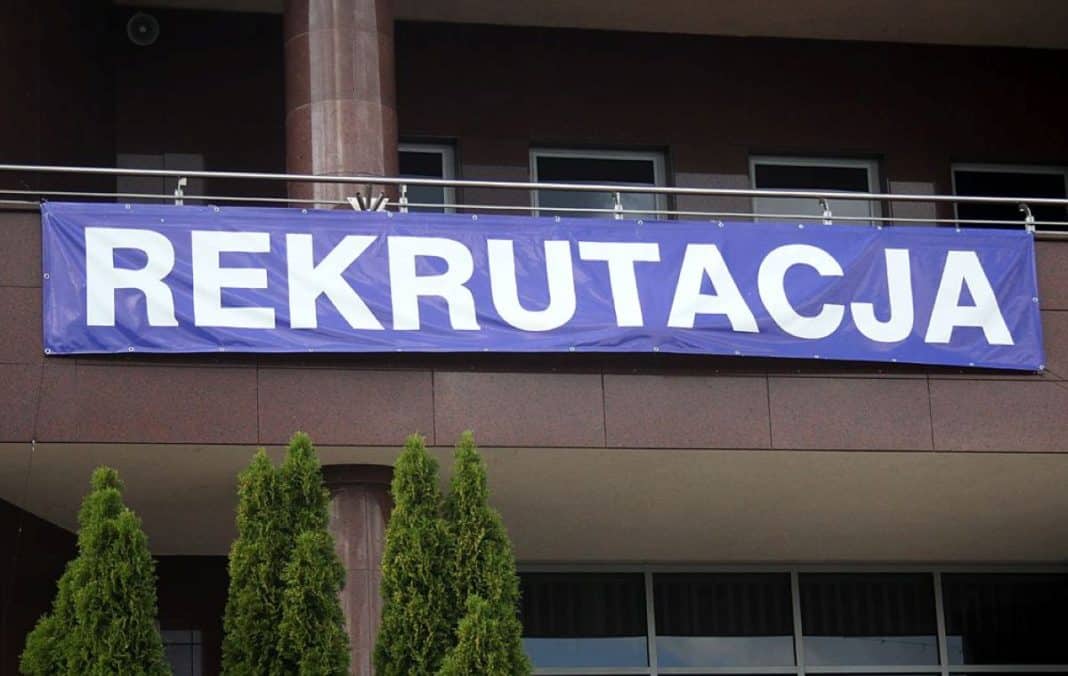 Baner z napisem 'Rekrutacja' na budynku uczelni, nad wejściem do budynku.
